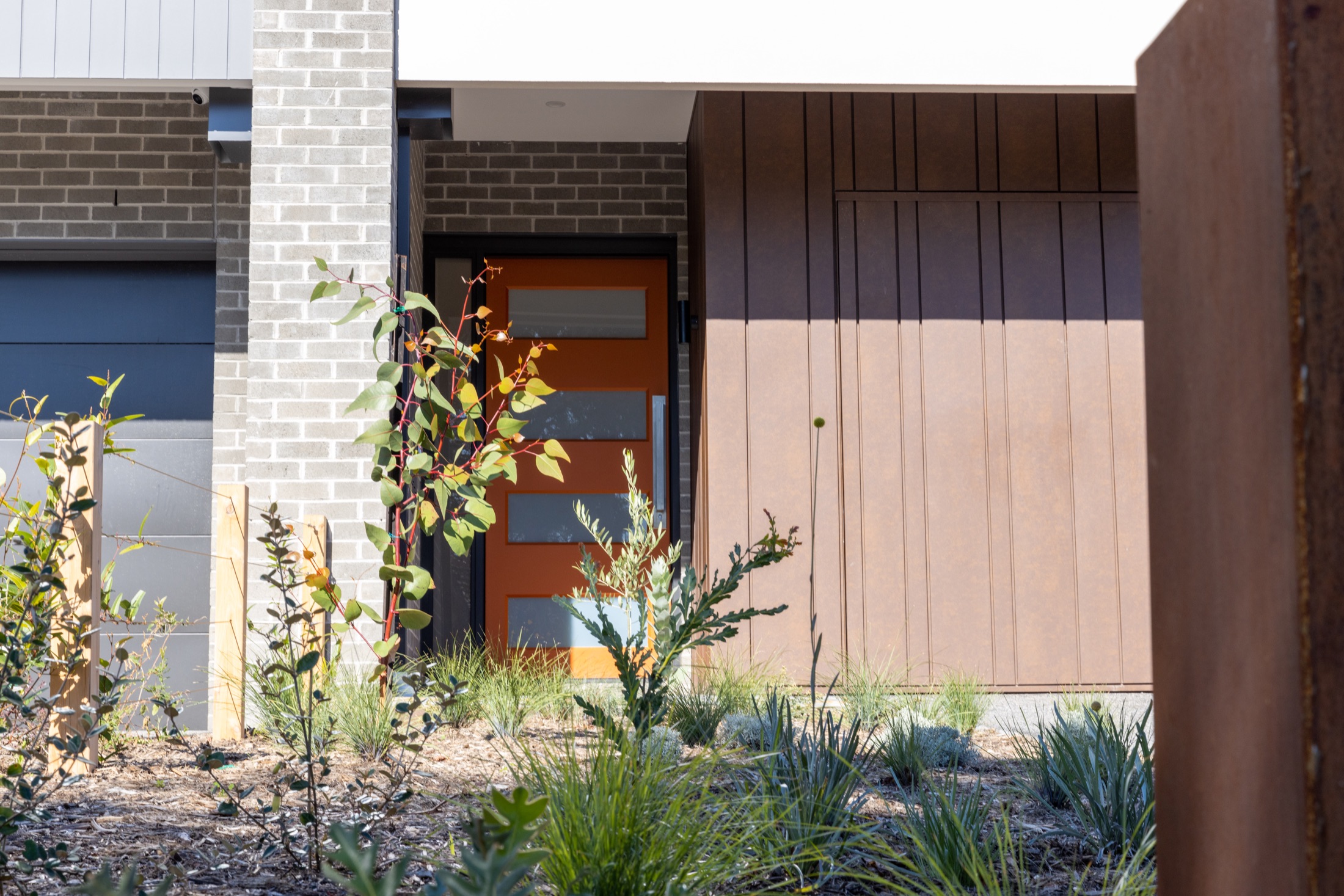 Landscaped entry to 20A Alicia Street, Hampton, with pale brick, bronze cladding and an orange front door